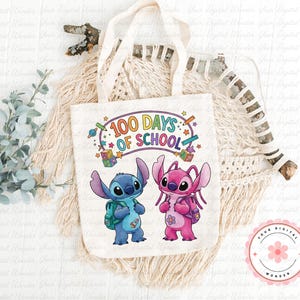 Op de afbeelding: Een witte draagtas met de tekst "100 Days of School" en stripfiguren. De tas heeft een blauw en roze buitenaards wezen met rugzakken. Het ontwerp bevat kleurrijke sterren, potloden en een planeet.
