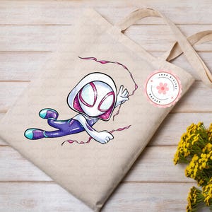 May include: Beige tote bag with a cartoon illustration of a superhero in a white and pink hooded costume, with purple and blue accents. The superhero is in a dynamic pose, with pink web lines. A pink floral sticker is on the bag.