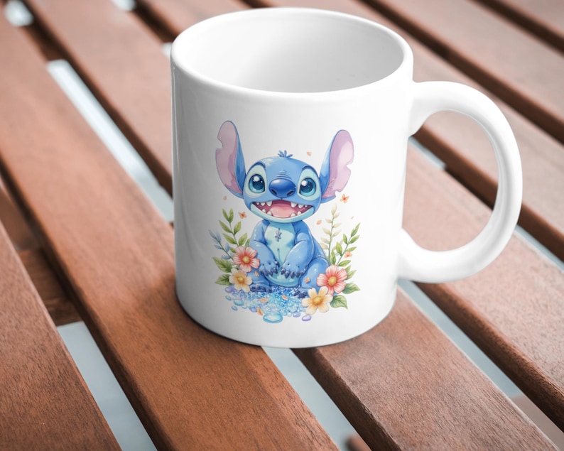 May include: White ceramic mug featuring a blue cartoon character with large ears and a wide smile, surrounded by colorful flowers and foliage. The character is sitting on a bed of blue water droplets. The mug has a curved handle.