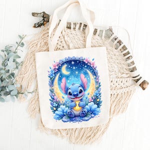 May include: A cream-colored tote bag featuring a blue cartoon character holding a glowing object, set against a crescent moon and starry night sky. The design is surrounded by flowers. The bag has two cream-colored handles.
