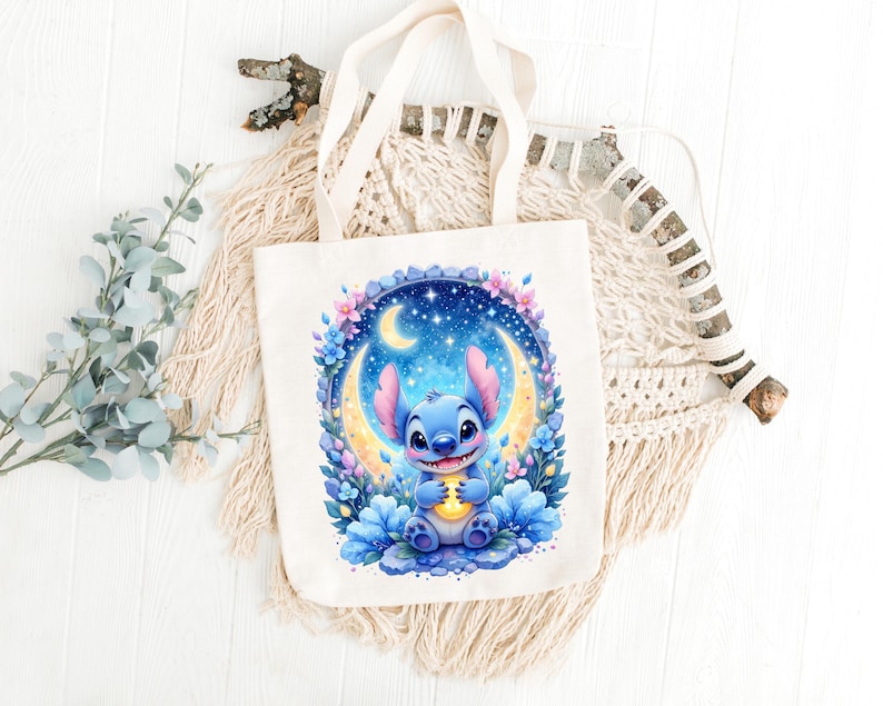May include: A cream-colored tote bag featuring a blue cartoon character holding a glowing object, set against a crescent moon and starry night sky. The design is surrounded by flowers. The bag has two cream-colored handles.