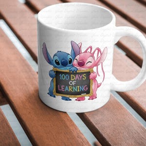 Op de afbeelding: Witte keramische mok met een blauw en roze cartoon alien paar dat een bord vasthoudt met de tekst "100 Days of Learning". De mok heeft een gebogen handvat en staat op een houten oppervlak.
