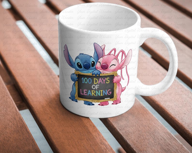 Op de afbeelding: Witte keramische mok met een blauw en roze cartoon alien paar dat een bord vasthoudt met de tekst "100 Days of Learning". De mok heeft een gebogen handvat en staat op een houten oppervlak.