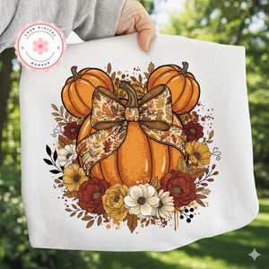 May include: White tote bag with a colourful autumn design. The design features three orange pumpkins, a large bow with a fall leaf pattern, and an arrangement of autumn-coloured flowers. The words "YOUR DIGITAL WONDER" are in a circle.