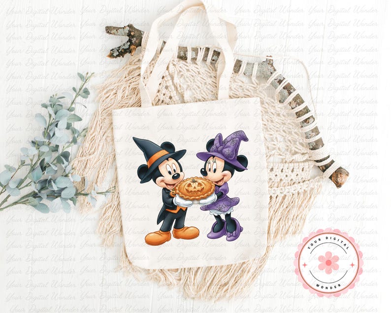 K&ouml;nnte beinhalten: Eine wei&szlig;e Canvas-Tragetasche mit einem Halloween-Motiv von Mickey und Minnie Mouse. Mickey tr&auml;gt einen schwarzen Hexenhut und h&auml;lt einen Kuchen. Minnie tr&auml;gt einen lila Hexenhut und ein Kleid. Die Tragetasche hat cremefarbene Griffe.