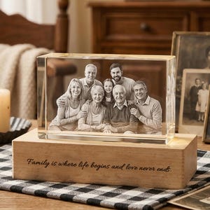 May include: A clear, rectangular photo block with a family portrait etched inside, resting on a wooden base. The base is engraved with the quote, "Family is where life begins and love never ends."