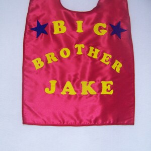 May include: Red satin cape with yellow felt lettering that reads "BIG BROTHER JAKE" and two blue felt stars.