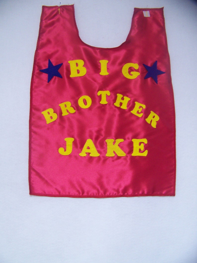 May include: Red satin cape with yellow felt lettering that reads "BIG BROTHER JAKE" and two blue felt stars.