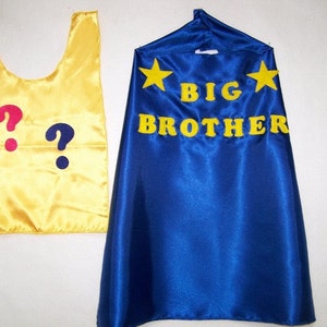 May include: A yellow cape with two question marks, one pink and one blue, and a blue cape with yellow stars and the text "BIG BROTHER" in yellow.
