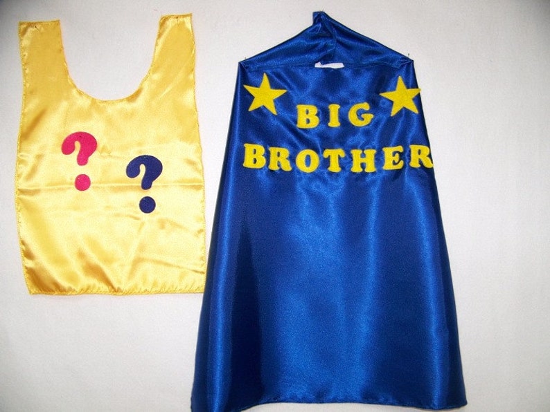 May include: A yellow cape with two question marks, one pink and one blue, and a blue cape with yellow stars and the text "BIG BROTHER" in yellow.