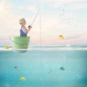 Puede incluir: Un niño con sombrero de paja y peto vaquero pescando desde un cubo verde en el océano. Un patito de goma flota cerca. Un pez dorado salta del agua y varios peces nadan por debajo de la superficie. Gaviotas vuelan en el cielo.