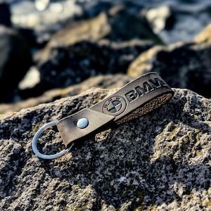 Può includere: Un portachiavi in ​​cuoio marrone con un anello portachiavi argentato e il logo BMW in rilievo.