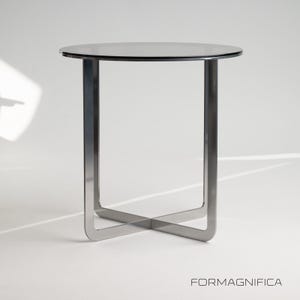Può includere: Un tavolino moderno con un piano rotondo in vetro scuro e una base in metallo spazzolato. La base presenta un design incrociato unico per la stabilità. Il tavolo è adatto a soggiorni o camere da letto. Altezza: circa 50 cm.