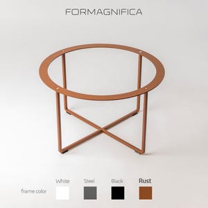 Puede incluir: Mesa de centro redonda de metal color óxido con tapa de cristal transparente. Diseño minimalista con base en forma de X y marco circular. La marca "FORMAGNIFICA" se muestra en la parte superior.