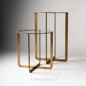 May include: Two gold-coloured metal side tables. One table is round, and the other is rectangular. Both tables have a clear glass top and a minimalist design. The tables are of different heights and sizes. The brand name "FORMAGNIFFICA" is printed at the bottom.