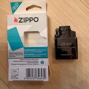 May include: A black Zippo single torch butane lighter insert and its white and teal cardboard packaging. The packaging features the Zippo logo, a barcode, and text including 'Single Torch Butane Lighter Insert' and 'Does not contain butane gas'.