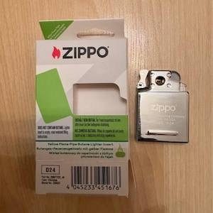 May include: A chrome Zippo pipe butane lighter insert and its white and green cardboard packaging. The packaging features the Zippo logo, a barcode, and text including Yellow Flame Pipe Butane Lighter Insert, D24, and Does Not Contain Butane.