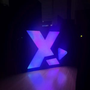 May include: A purple and blue illuminated sign with the letter "X" and a play button.