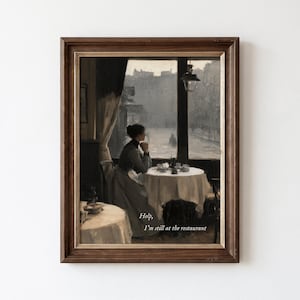 May include: A framed wall art print depicting a person sitting at a round table in a dimly lit restaurant, looking out a window at a rainy street scene. The text "Help, I'm still at the restaurant" is printed in white at the bottom of the image.