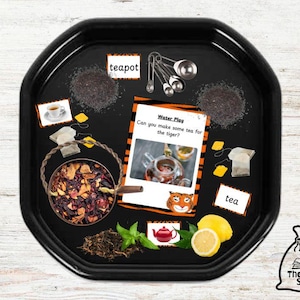 May include: A black plastic tray with a variety of items for a pretend play tea party. The tray includes loose leaf tea, tea bags, a teapot, measuring spoons, lemons, and a card with the text "Water Play Can you make some tea for the tiger?"