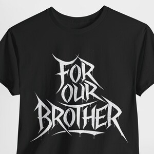 Può includere: Maglietta nera con una stampa grafica bianca che dice "For Our Brother" in un font stilizzato.