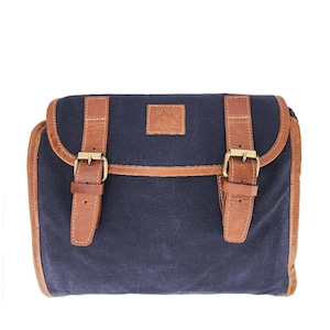 Op de afbeelding: Een marineblauwe messenger bag met bruine leren afwerking en riemen. De tas heeft twee leren riemen met messing gespen en een kleine leren patch met een berglogo. De tas is rechthoekig en heeft een klepsluiting.