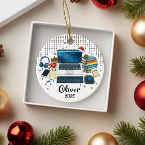 Pu&ograve; includere: Ornamento natalizio rotondo con un tema di programmazione informatica. Il design include un laptop, una tastiera, un mouse, cuffie, una tazza di caff&egrave; e libri. Il nome "Oliver" e l'anno "2025" sono stampati.