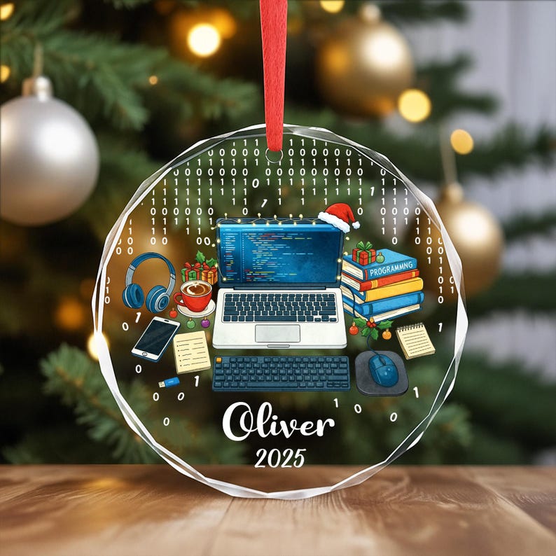 Pu&ograve; includere: Un ornamento natalizio rotondo e trasparente con un nastro rosso. L'ornamento presenta un laptop, una tastiera, un mouse, cuffie, una tazza di caff&egrave; e libri. Il nome "Oliver" e l'anno "2025" sono stampati.