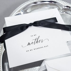 May include: A white card with black text and a black ribbon tied around it. The text reads "To my mother on my wedding day".