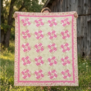 Puede incluir: Un edredón hecho a mano con un fondo verde claro y patrones florales y geométricos rosas. El edredón tiene un borde floral rosa y se sostiene frente a una estructura de madera rústica y hierba verde.