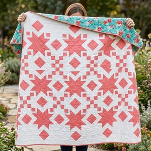 Puede incluir: Un edredón hecho a mano con un fondo blanco y un patrón de estrella coral. El borde del edredón presenta un estampado floral en tonos de rojo, rosa y verde sobre un fondo turquesa. El edredón se sostiene, mostrando su diseño y construcción.