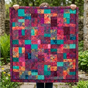 May include: A patchwork quilt in shades of teal, magenta, and burgundy, with a dark purple border. The quilt is made up of various squares and rectangles. The quilt is being held up by a person. The quilt's design is a mix of geometric shapes and patterns.