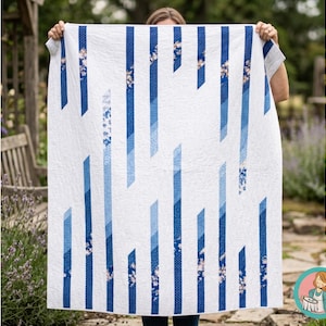 Puede incluir: Un edredón blanco con un diseño geométrico de rayas azules y detalles florales. El edredón presenta diferentes tonos de azul en un patrón moderno y abstracto. El edredón se sostiene, mostrando su tamaño y diseño.