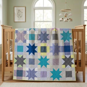 Puede incluir: Un edredón de bebé hecho a mano con un patrón de estrellas en tonos de azul, verde, morado y amarillo. El edredón está sobre una cuna de madera. Un oso de peluche está dentro de la cuna. Un móvil con ovejas y nubes cuelga encima.