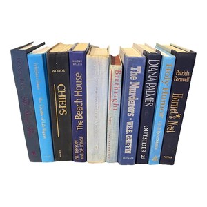 May include: A collection of 14 blue and black hardcover books with various titles, including "The Beach House", "Chiefs", "Birthright", "The Murderers", "Outsider", "Hornet's Nest", and "Holy Humor".
