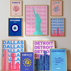May include: A collection of framed art prints featuring city and travel-themed designs. The prints showcase iconic landmarks and destinations, including New York, Chicago, and Venice, in vibrant colors. The artwork is displayed on a wooden floor.