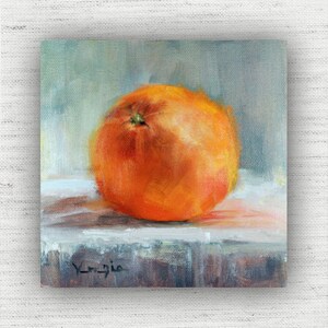 May include: An oil painting of a vibrant orange fruit, likely an orange or tangerine, set against a soft, blurred background. The artwork features warm orange hues with subtle highlights, creating a realistic depiction of the fruit. The painting is signed in the lower left corner.
