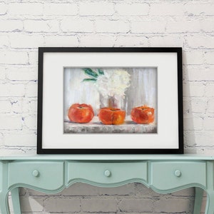 May include: A framed still life painting featuring three vibrant orange fruits, possibly persimmons, arranged on a shelf. A vase of white flowers is visible in the background. The artwork is displayed on a light blue table against a white brick wall.