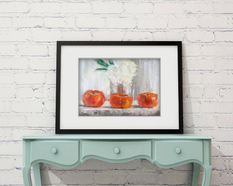 May include: A framed still life painting featuring three vibrant orange fruits, possibly persimmons, arranged on a shelf. A vase of white flowers is visible in the background. The artwork is displayed on a light blue table against a white brick wall.