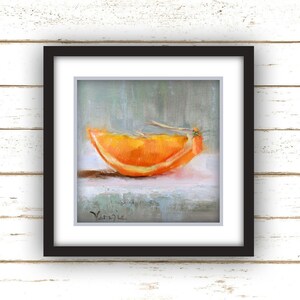 May include: A framed painting of a vibrant orange slice. The artwork features a close-up view of the orange segment, showcasing its bright orange color and textured surface. The painting is set against a soft, muted background, and is framed in a black square frame.