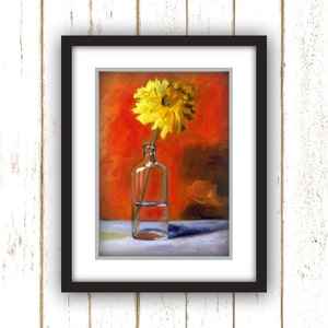 May include: A framed painting of a yellow flower in a clear glass bottle. The flower is centered, with a vibrant orange background. The painting is in a black frame, set against a white wooden background.