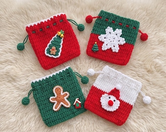 Puede incluir: Cuatro bolsas de ganchillo cuadradas con cordón y motivos navideños. Una bolsa roja con un árbol y un hombre de jengibre, una verde con un copo de nieve blanco, una verde con un hombre de jengibre y una blanca y roja con una cara de Santa.