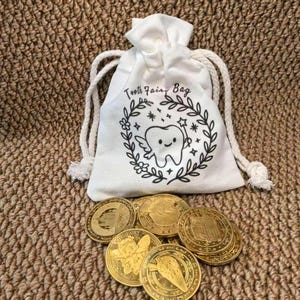 May include: A white drawstring bag with the text "Tooth Fairy Bag" and a cartoon tooth illustration, surrounded by a wreath. Several gold coins are scattered below the bag, each with a unique design.
