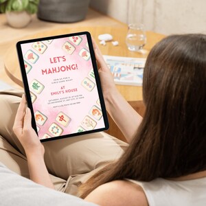 May include: A tablet displays a pink invitation for a Mahjong game night. The invitation features decorative Mahjong tiles around the border and the text "LET'S MAHJONG!" and "JOIN US FOR A GIRLS GAME NIGHT AT EMILY'S HOUSE".
