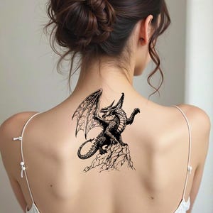 May include: Black dragon tattoo design on a person's back. The dragon is perched on a rocky surface with its wings spread. The tattoo is detailed with scales and intricate wing patterns. The dragon is facing to the left.