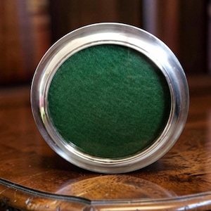 May include: A circular picture frame with a polished silver-toned metallic border and a deep forest green felt insert. The frame features a smooth, reflective finish on the outer rim and a simple, clean design that holds the solid green centre.