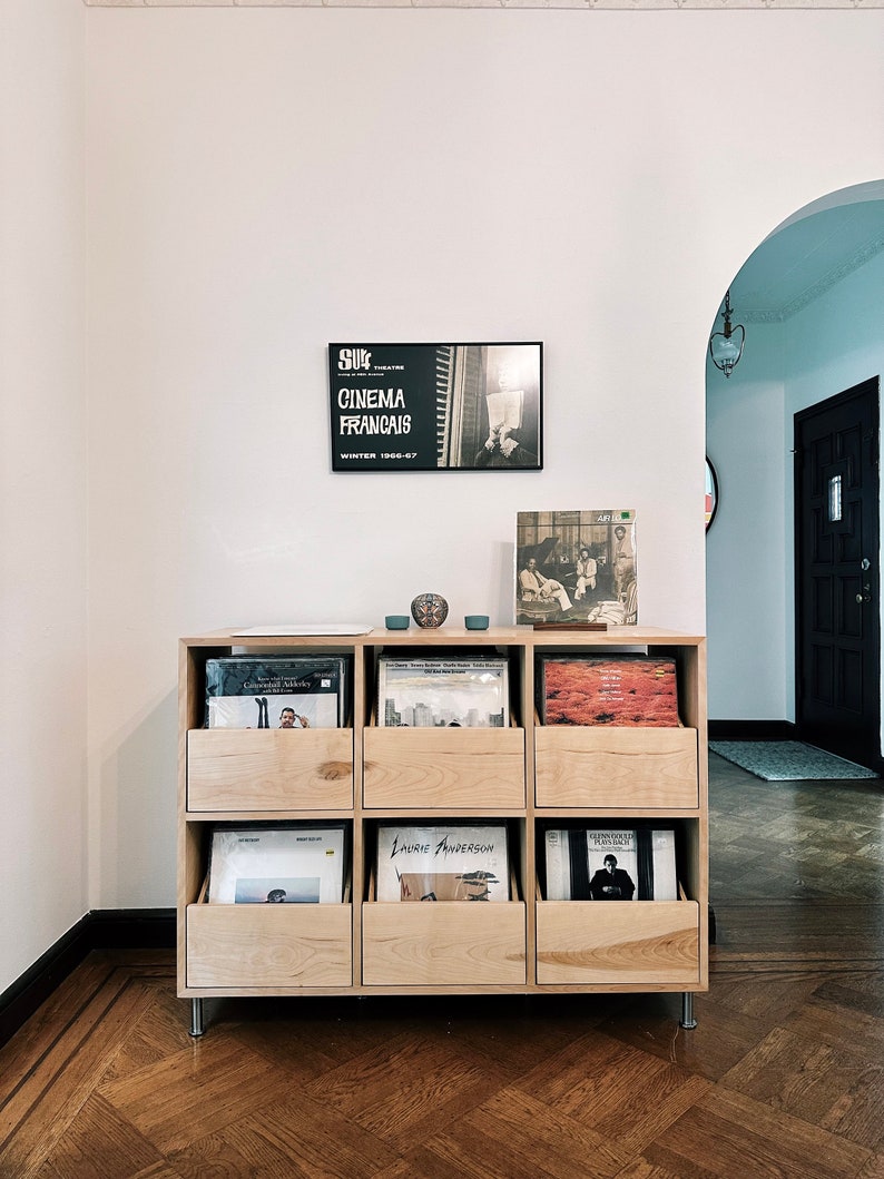 A custom natural birch 6-drawer cabinet in a client's home with various vinyl records inside the drawers. There is a framed print on the wall behind; two small blue bowls and an LP on the top of the unit. The floors are wood.