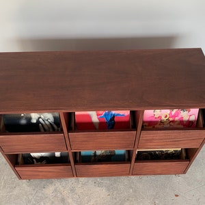 A bird's eye view of a six-drawer record storage cabinet in a medium brown stain with vinyl records inside the drawers. The legs are chrome.
