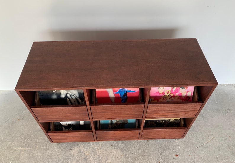 A bird's eye view of a six-drawer record storage cabinet in a medium brown stain with vinyl records inside the drawers. The legs are chrome.