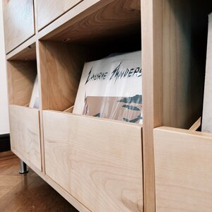 A close up photo of a custom natural birch cabinet's closed drawer with records inside a client's home. There is a Laurie Anderson LP peeking out.
